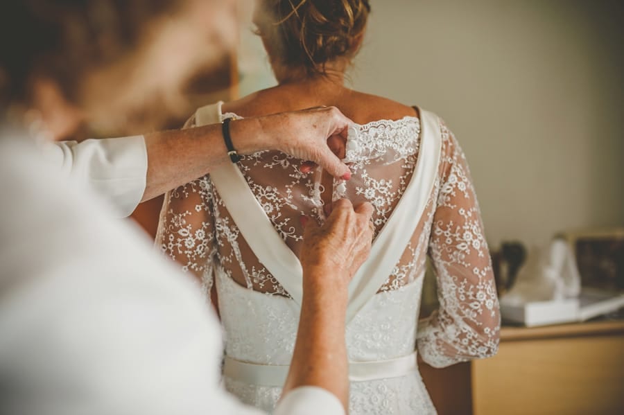 The brides mother fastens the buttons on the back of the brides dress