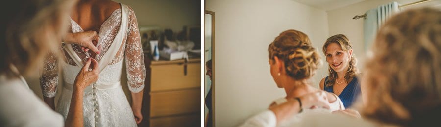 A bridesmaid watches the brides mother fasten the buttons on the back of the brides dress