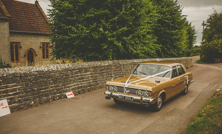The bride and her father arrive at the church in an old car made by Ford from the 1970s
