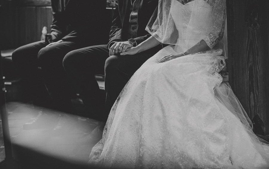The groom holds the hand of the bride as they sit in church and listen to the wedding ceremony