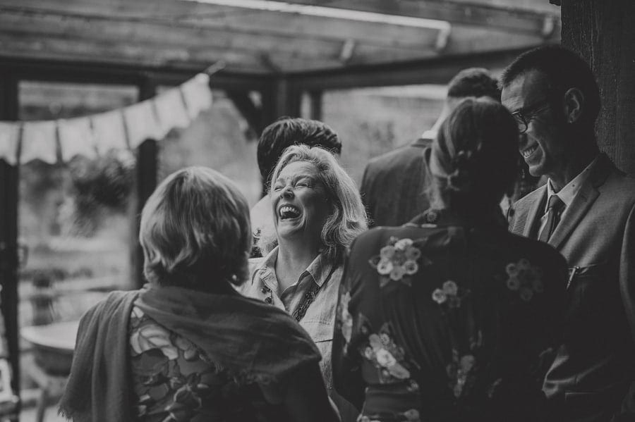 A wedding guest closes her eyes and laughs as she talks to friends at Yarlington barn in Somerset