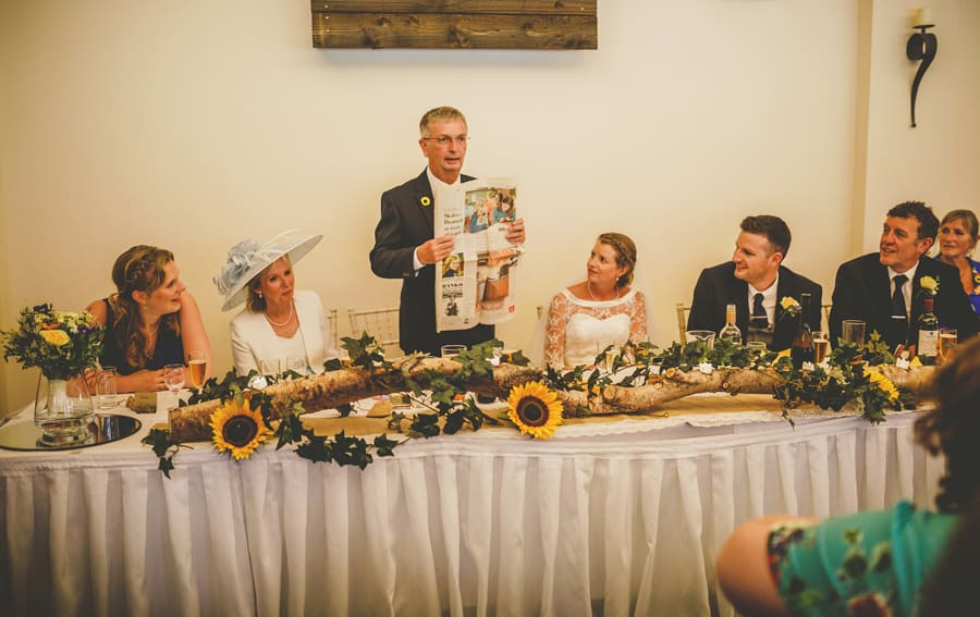 The bride's father holds a newspaper up and delivers his speech to the wedding party at Yarlington barn in Somerset