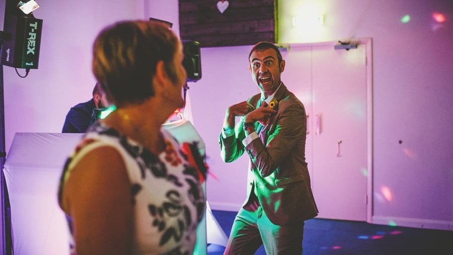 A wedding guest dancing with his wife makes a gesture to her on the dancefloor at Yarlington barn
