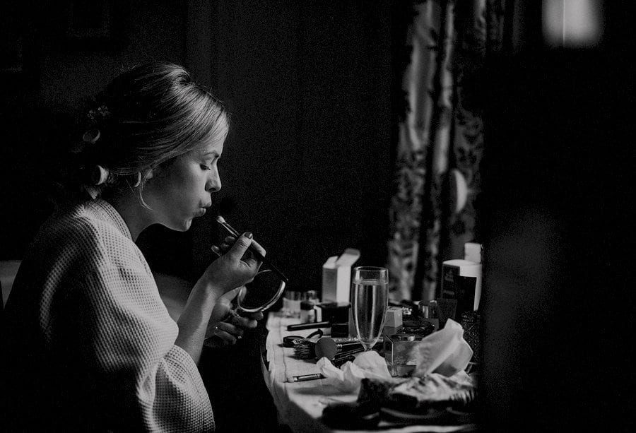 The bride blows her make up brush as she sits in front of the window