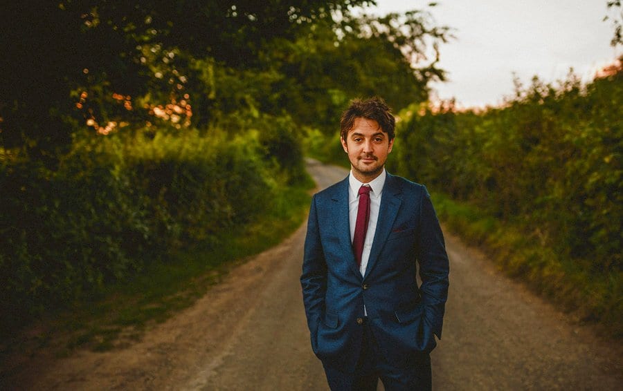 The groom poses for a photograph along a country lane outside Penny Square Barn