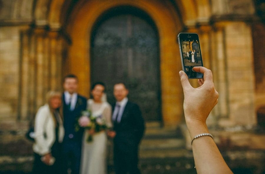 A lady takes a photograph of the bride and groom on her phone