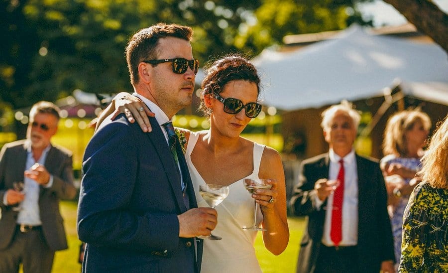 The bride and groom drink champagne together on the lawn