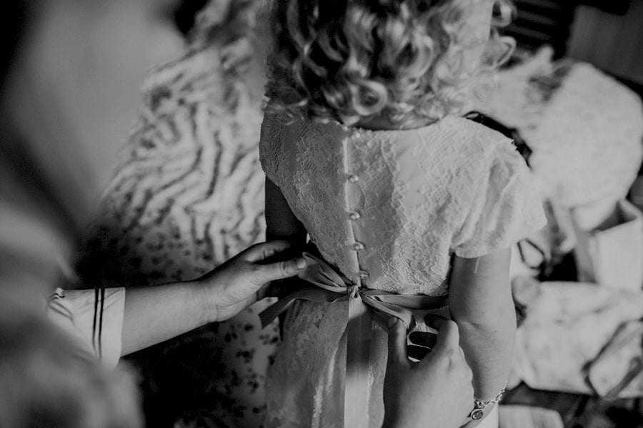 The bride ties the flower girls straps on the back of her dress at Over Barn