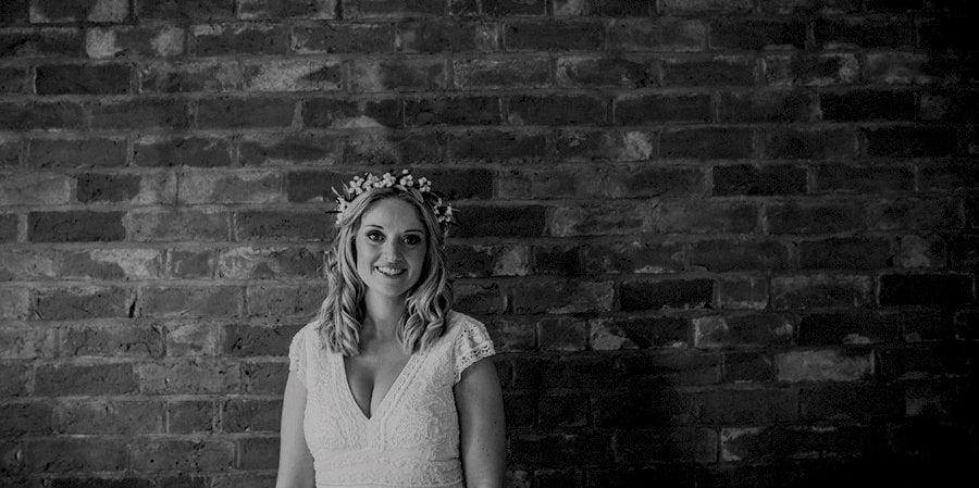 The bride posing for a photograph against a large brick wall