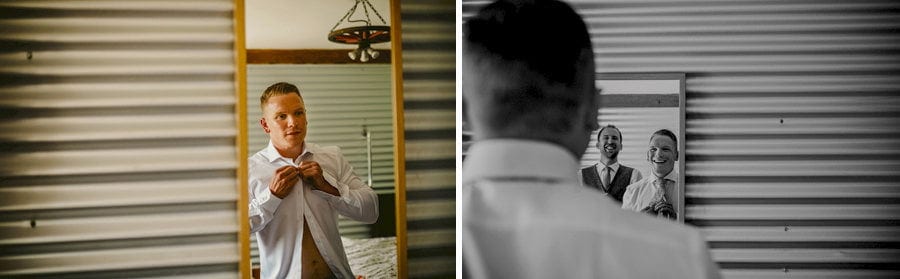 The groom fastens a button at the top of his shirt as he looks in the mirror