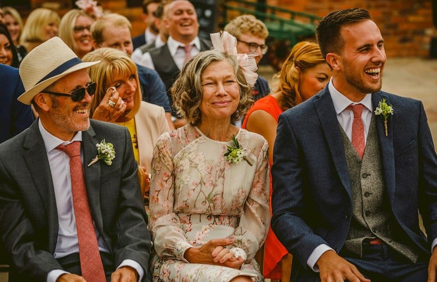 The grooms mother and father and the best man laugh during the outdoor wedding ceremony
