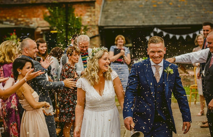 The bride and groom walk down the aisle together and are showered in confetti that is thrown by wedding guests at Over Barn in Gloucestershire