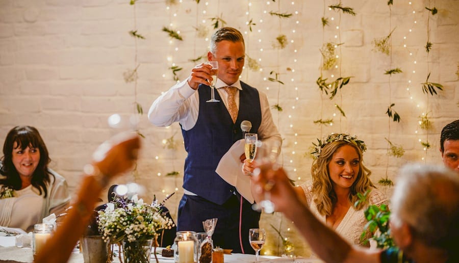 The groom raises his glass with friends and family as he makes a toast to his wife in the barn