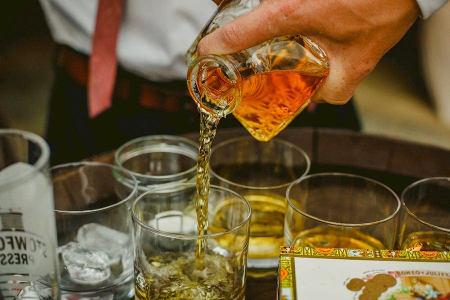 The groom pours brandy into glasses in the courtyard at Over Barn