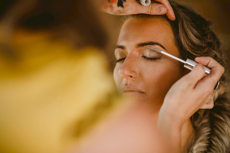 A makeup artist carefully applies mascara onto the eyebrows of one of the bridesmaids in the cottage at Yurt retreat