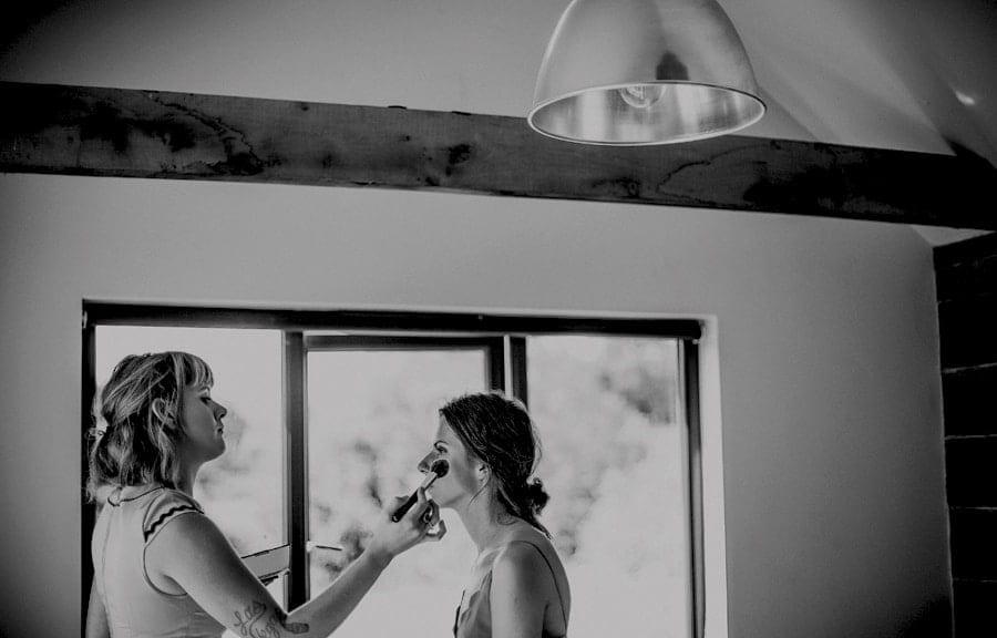 Makeup is applied to the brides face by the makeup artist next to a large window in the cottage