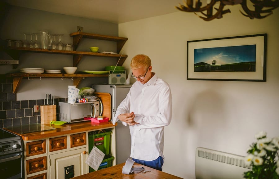 The groom puts on his cufflinks in the kitchen of the cottage