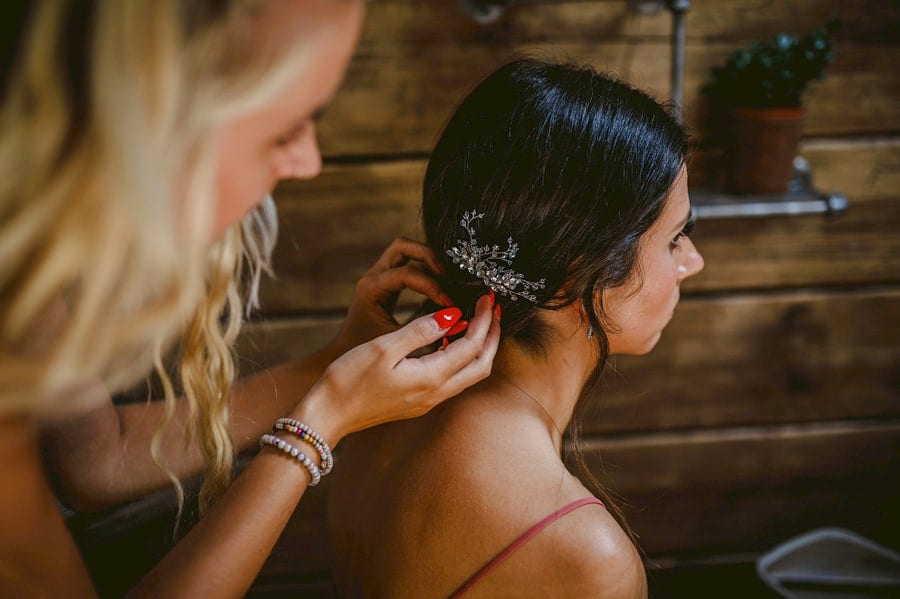 The hairdresser places a clip on the back of the brides hair as she sits down in the cottage