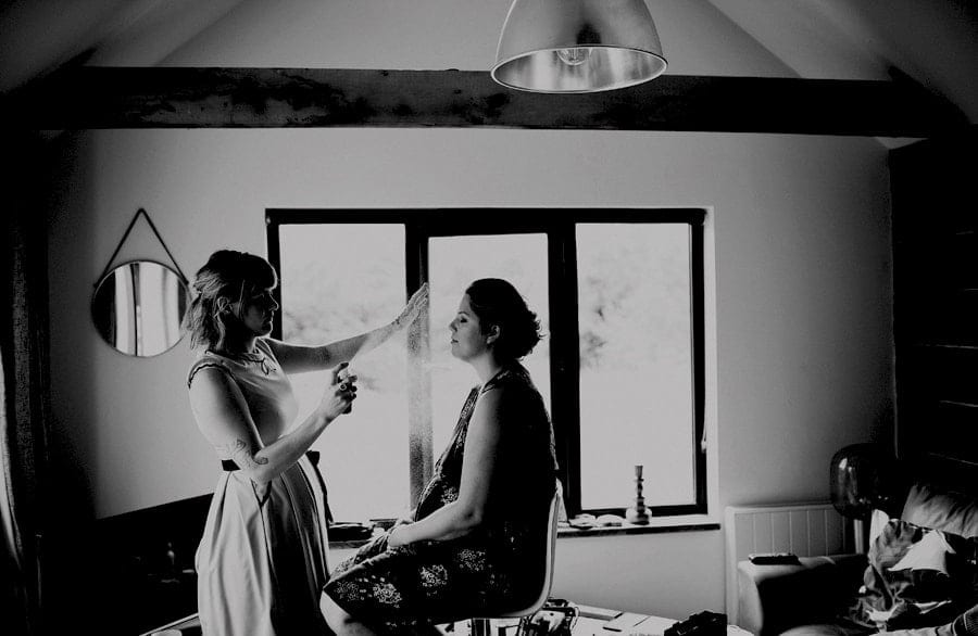 The makeup artist sprays a bridesmaid face as she sits down in the cottage