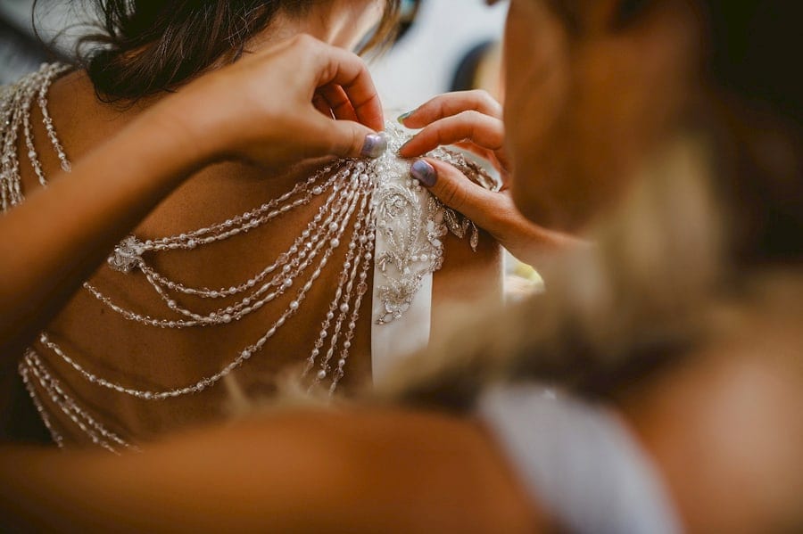 A bridesmaid fastens the back of the brides dress