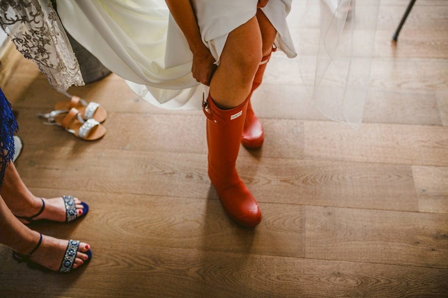 The bride puts on her new red wellington boots in the kitchen of the cottage