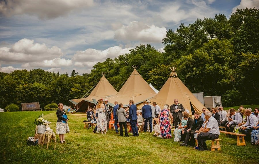 Wedding guests gather in the field next to the large tipi for the outdoor wedding ceremony at Yurt retreat in Crewkerne