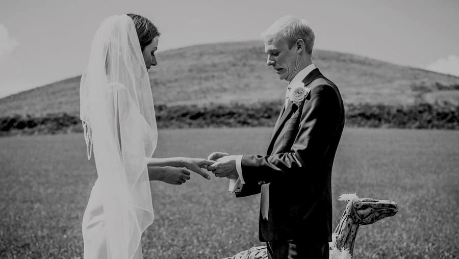 The groom places a ring on the finger of the bride during the outdoor wedding ceremony