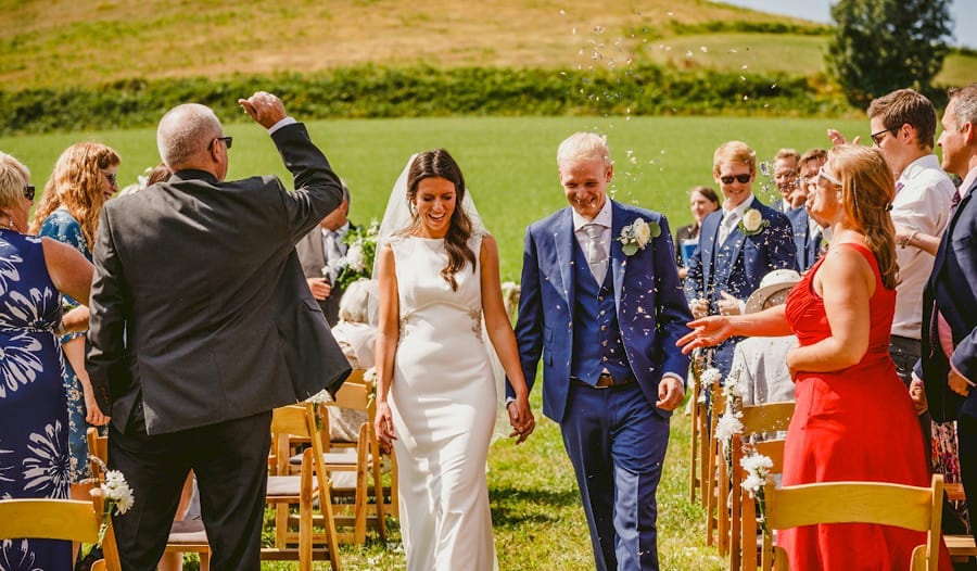 The bride and groom walk down the aisle of the outdoor ceremony as guests throw confetti in the air