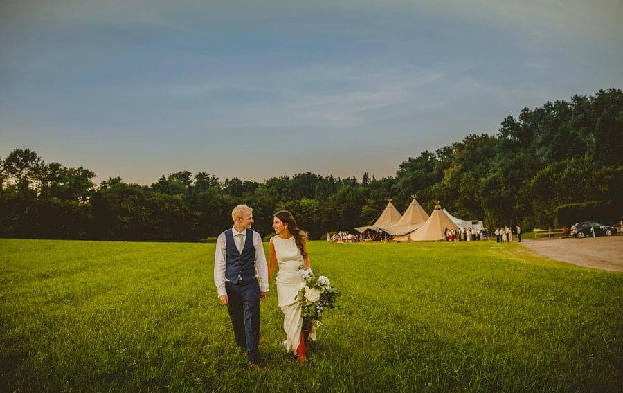 The bride and groom look at each other and walk hand in hand across the field at Yurt Retreat