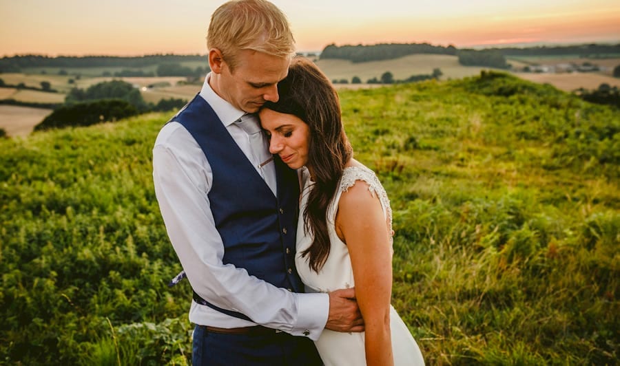 The bride puts her head on the grooms chest and closes her eyes on top of the hill at yurt retreat in Crewkerne, Somerset