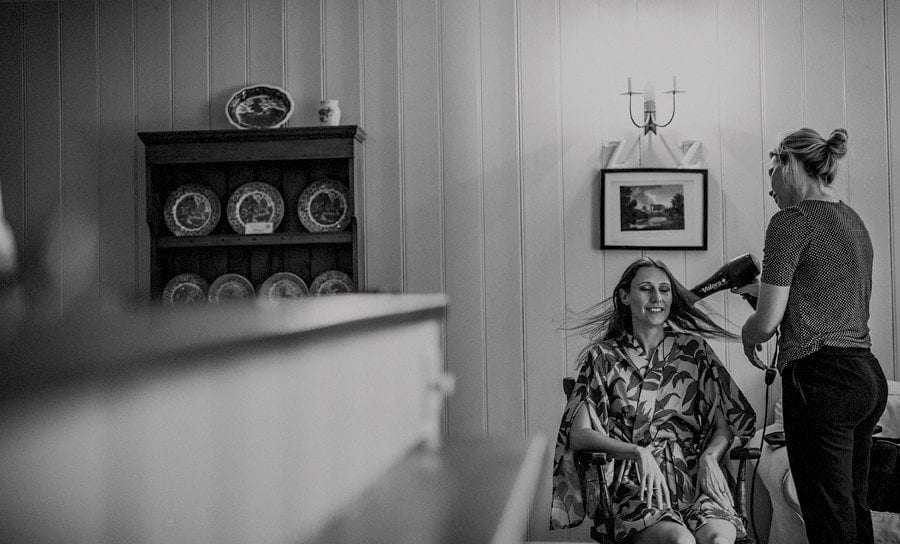 The hairdresser blow dries the brides hair as she sits in a chair