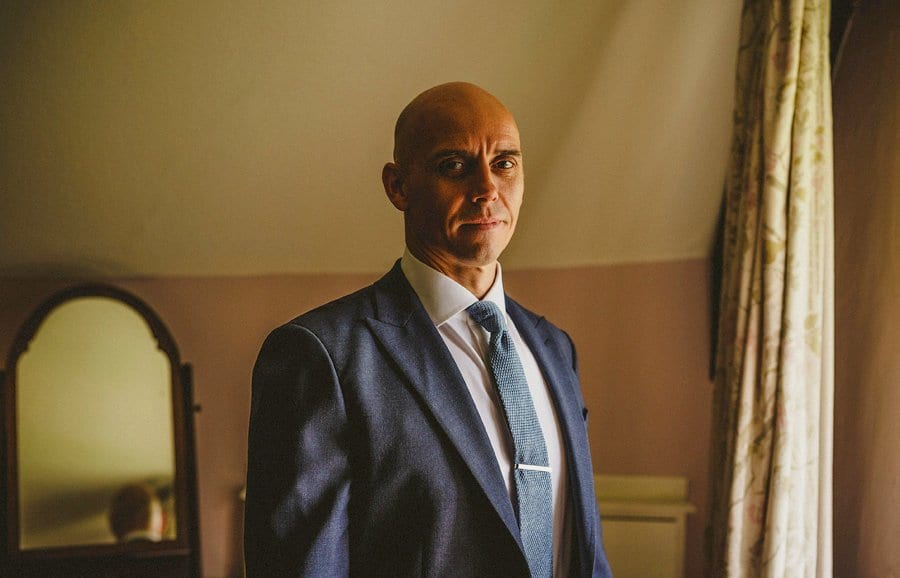 The groom poses for a photograph in one of the bedrooms at Abbey House Gardens