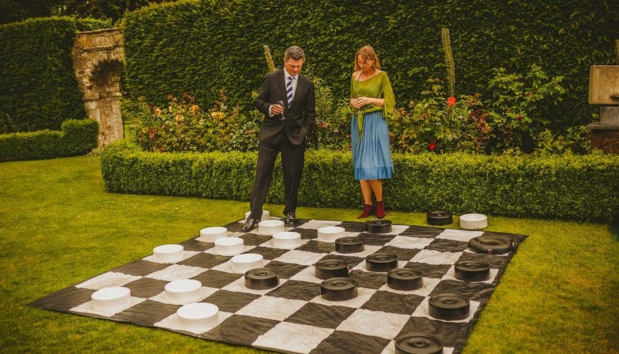 Two wedding guests look at a large draughts board on the grass at Abbey House Gardens