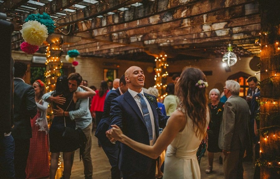 The groom holds his brides hands on the dancefloor and smiles at her