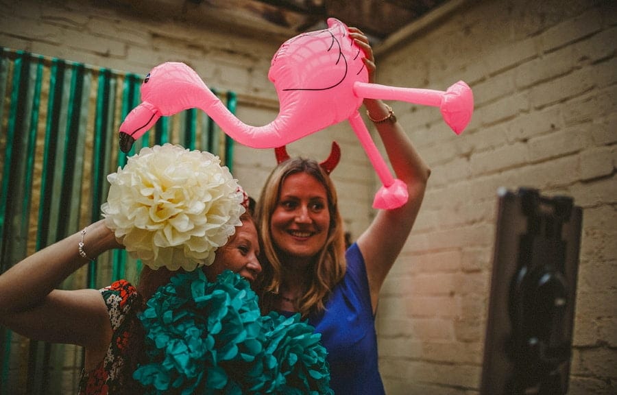 Two ladies hold up an inflatable pink flamingo and pose for a photograph in the photo booth