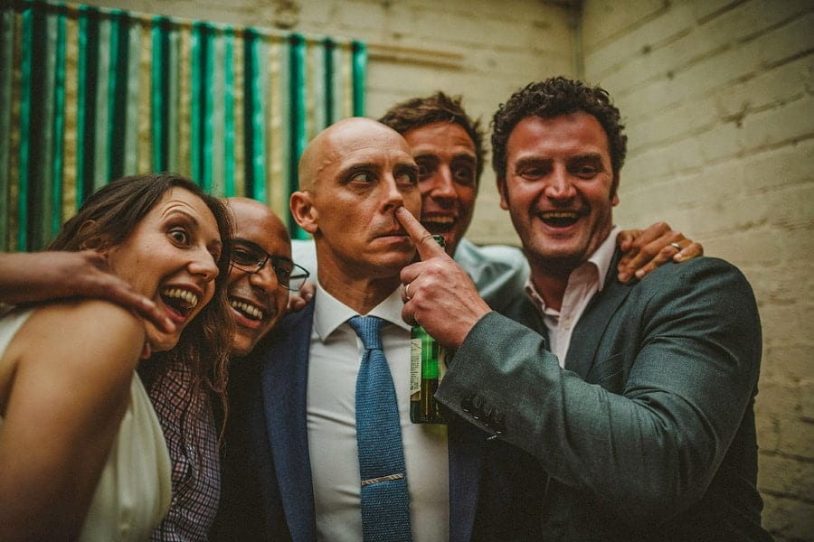 A wedding guest places his finger to the grooms nose and laughs as they pose for photographs in the photo booth