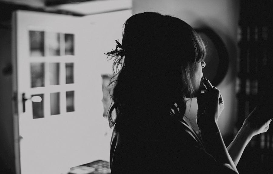 A bridesmaid puts on lipstick in the kitchen of the cottage