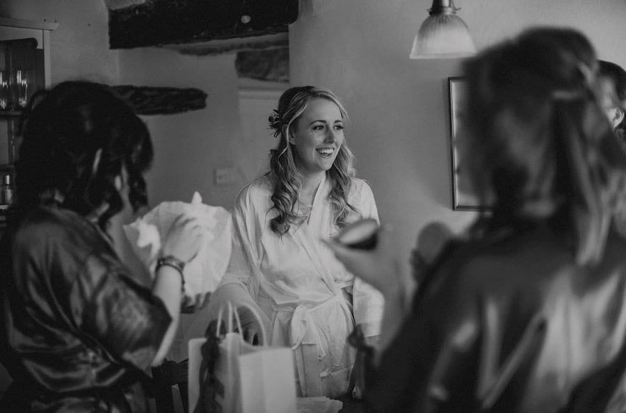 The bridesmaid smiles as she watches her bridesmaids open gifts in the kitchen
