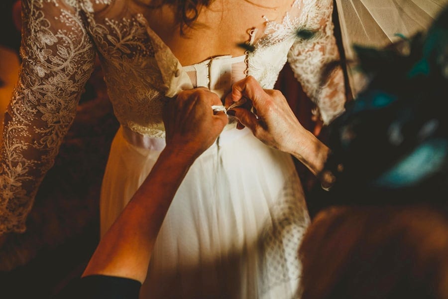 The mother of the bride ties the back of her daughters wedding dress in one of the bedrooms of the cottage
