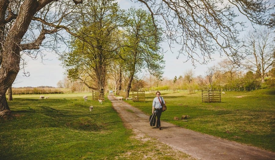 A member of the wedding band walks down the path towards the Church with a guitar in his right hand