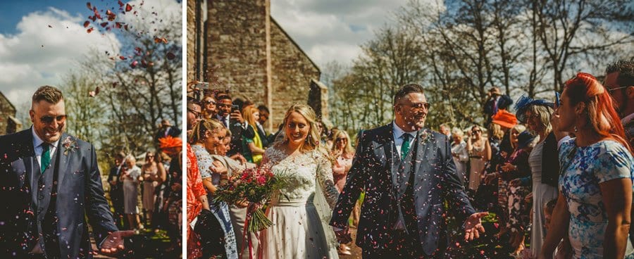 The bride and groom walk out of the church and are showered in confetti