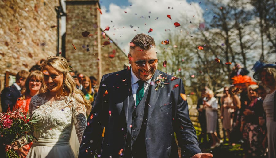 The groom catches confetti that has been thrown over him by wedding guests outside the Church