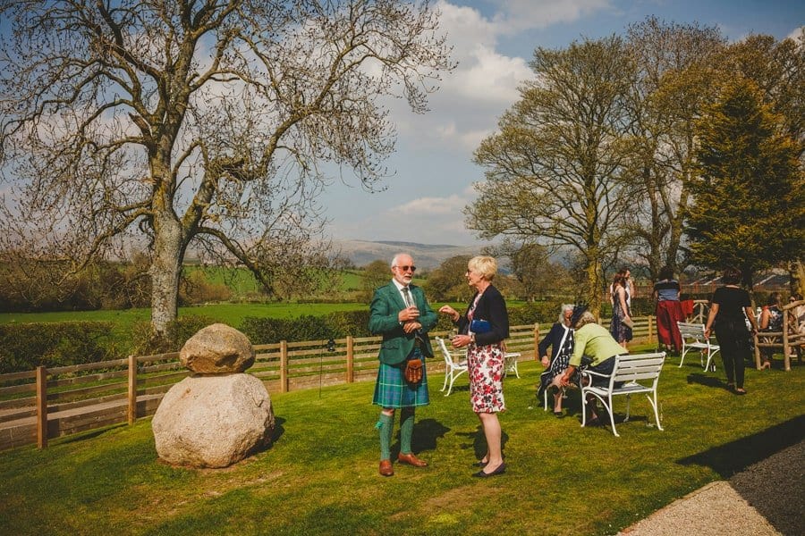 Wedding guests drink champagne and chat to one another in the garden at Eden Barn
