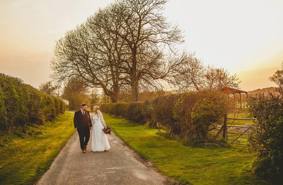 The bride and groom walk along the lane outside Eden Barn as the sunsets