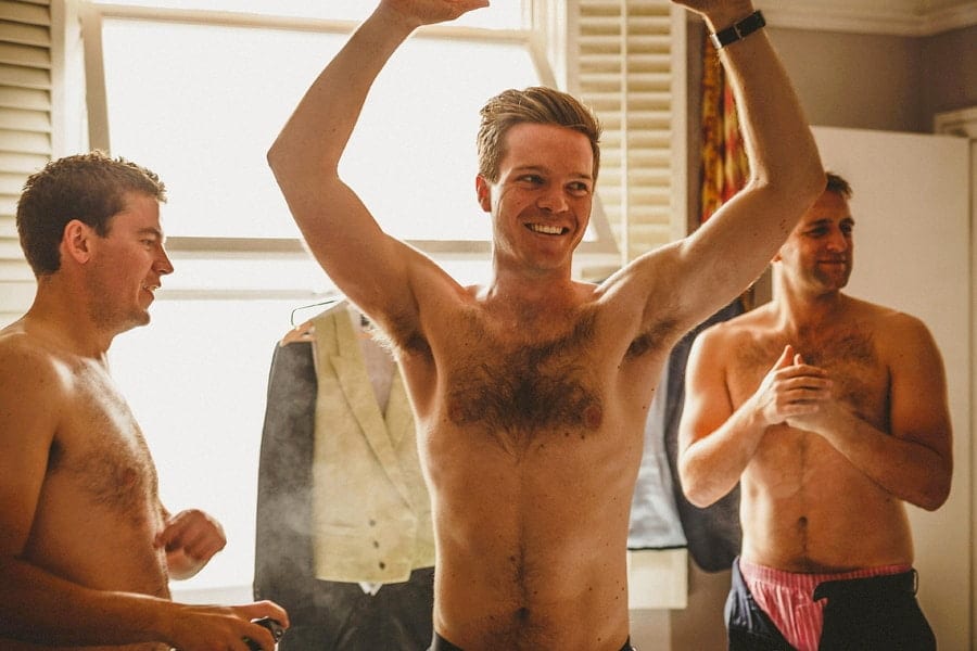 The groom raises his arms and his best man sprays deodorant on his chest