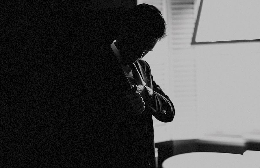 The groom puts his jacket on next to the window of the hotel