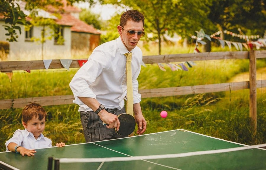 A wedding guest plays table tennis with his young son watching