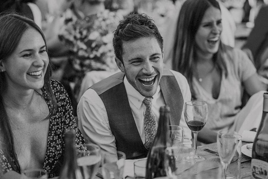 A wedding guest laughs as he sits at the wedding table in the marquee.