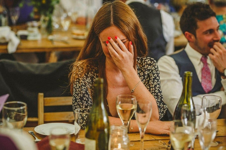 A wedding guest holds her hand to her face and laughs