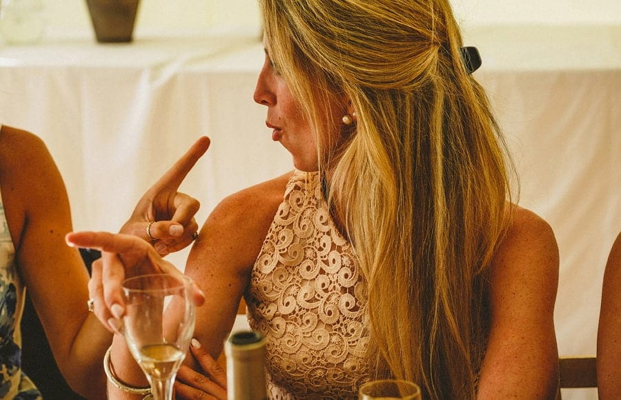 A wedding guest laughs with a friend at the wedding table in the marquee